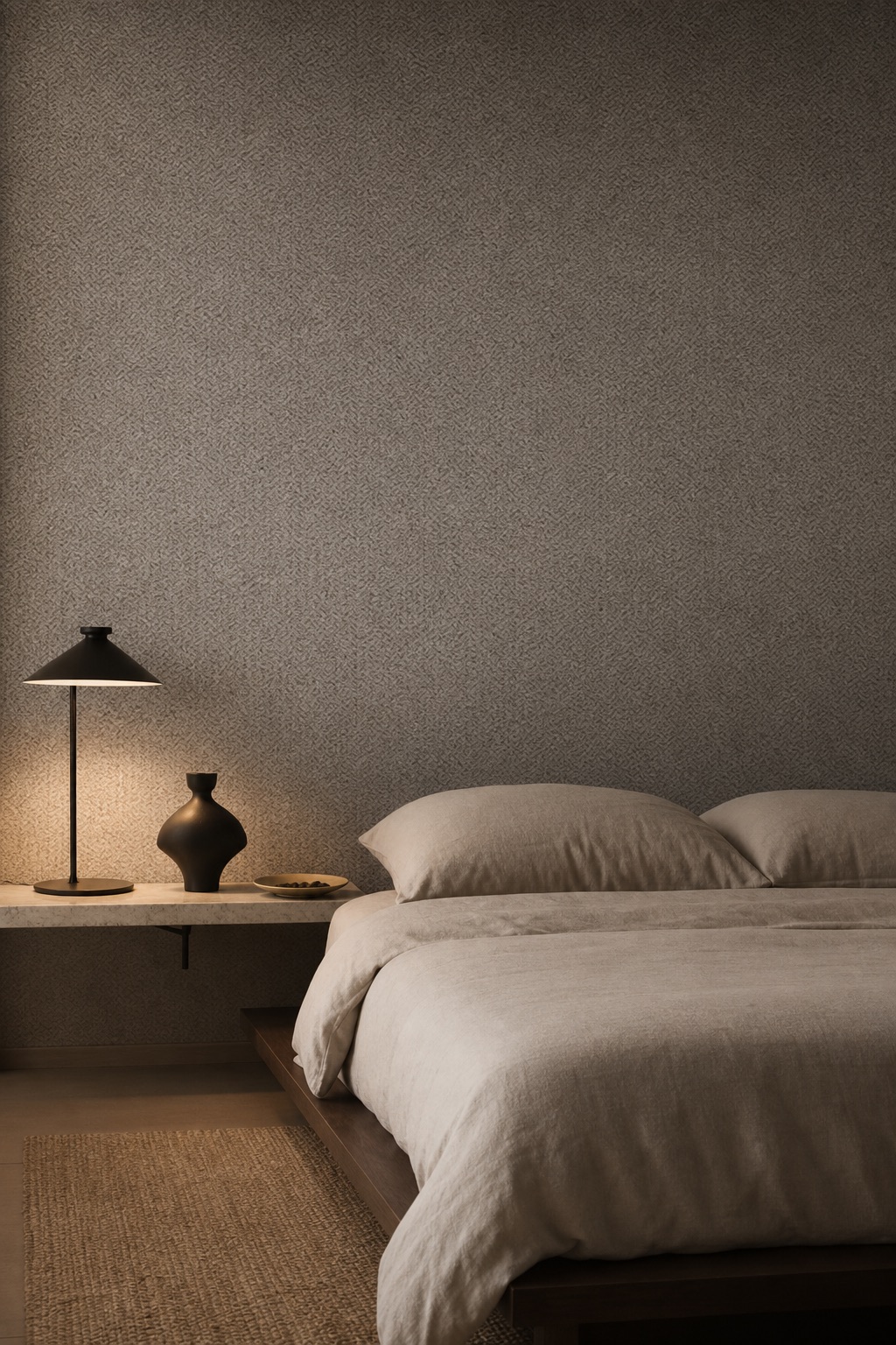 Minimal bedroom with Slate Chevron charcoal geometric grasscloth headwall, undyed linen bedding, and warm table lamp at night