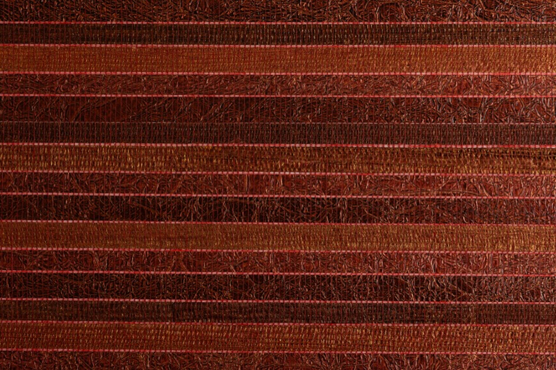 Close-up of Garnet Reed red grasscloth wallpaper showing deep burgundy-red horizontal reed bands with bright crimson accent stripes and matte crinkled filament surface