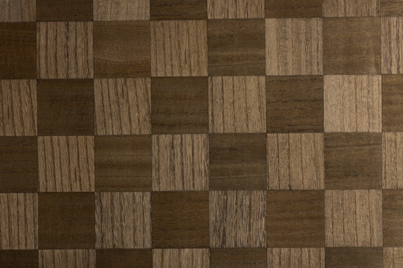 Close-up of Walnut Checker walnut veneer wallpaper showing alternating dark walnut-brown and warm caramel square tiles with visible horizontal grain lines