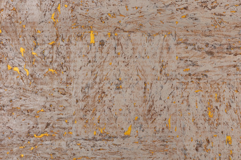 Close-up of natural cork wallpaper with warm greige-taupe base and scattered amber-gold foil inlays, horizontal fibrous bark striations visible across the full surface