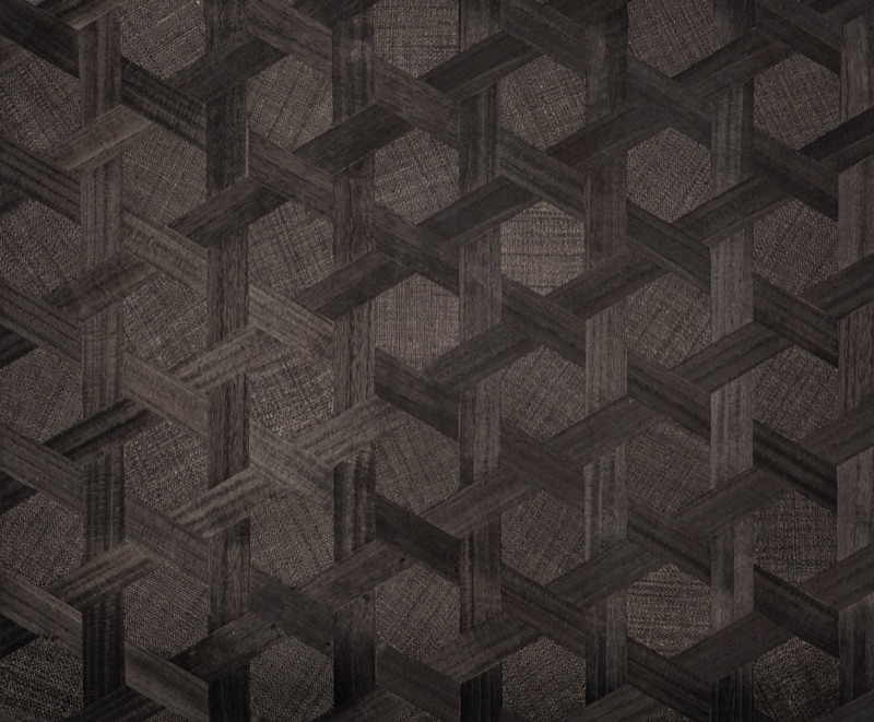 Образец чёрных травяных обоев Obsidian Hex с шестиугольным плетением: крупный взаимосцепляющийся шестиугольный корзиночный рисунок с чередующимися гладкими полосами с эффектом зерна и тонкими секциями с клетчатой фактурой в тёмном угольно-коричневом цвете